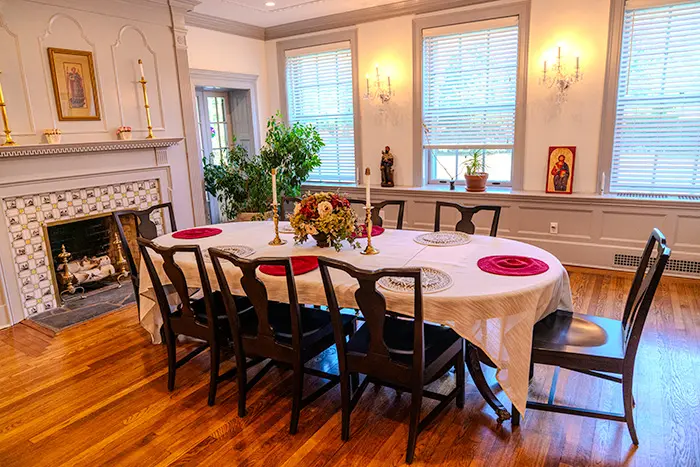 Dining room with a table set for eight guests in front of a decorative fireplace while windows let in natural light